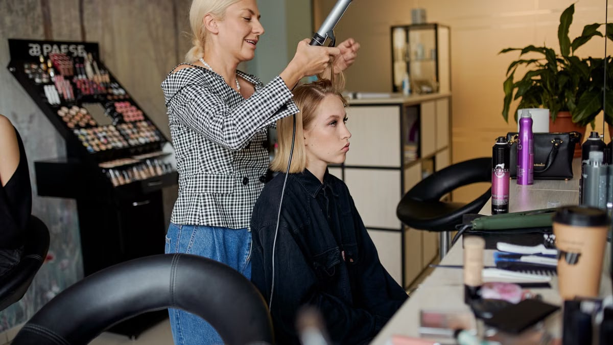 Side view of adult hairstylist straightening hair of client with iron in hairdressing salon